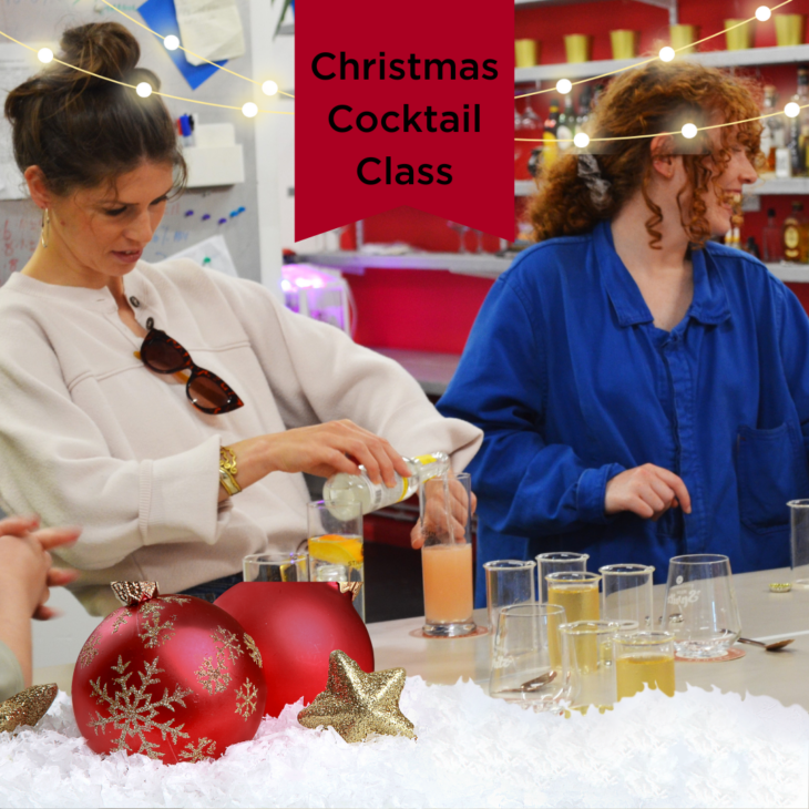 Two people at a festive cocktail class. One pours a drink, the other sits with glasses in front. The setting is decorated for Christmas with red ornaments, snow, and a banner reading "Christmas Cocktail Class.